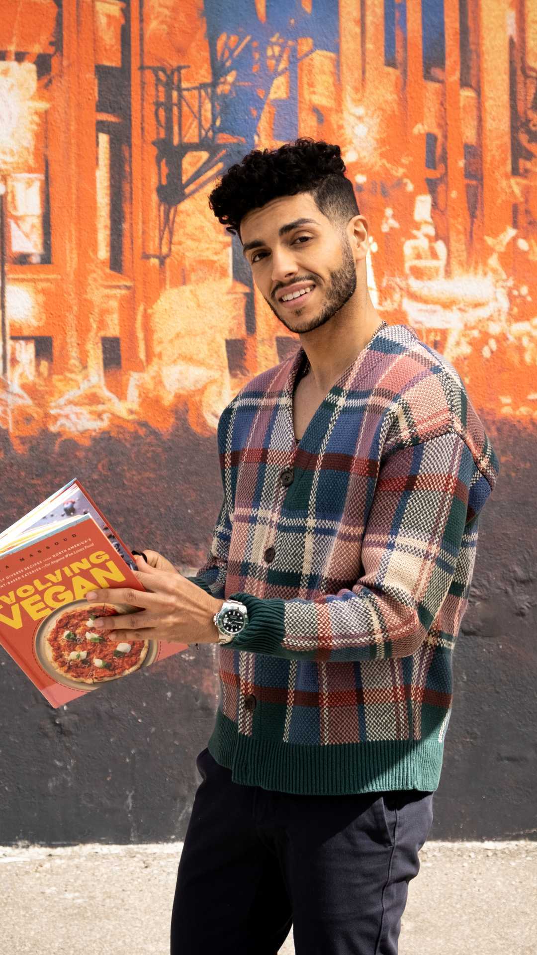 Mena Massoud | Aladdin actor Mena Massoud holding his Evolving Vegan cookbook